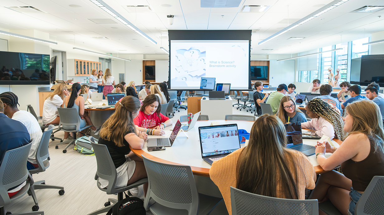 students working in a classroom sitting around circular tables