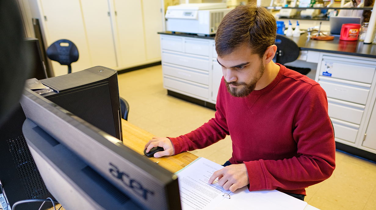 male student working on a computer with paper in front of him