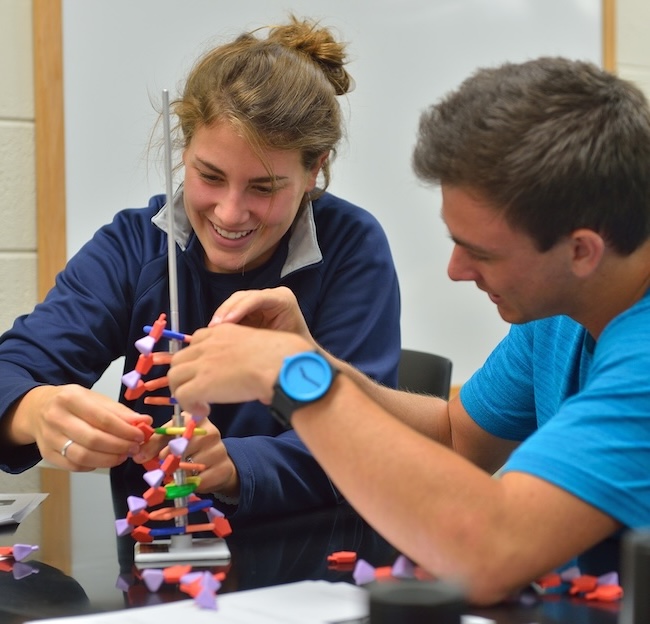 two students smiling and using a hands on demonstration of dna