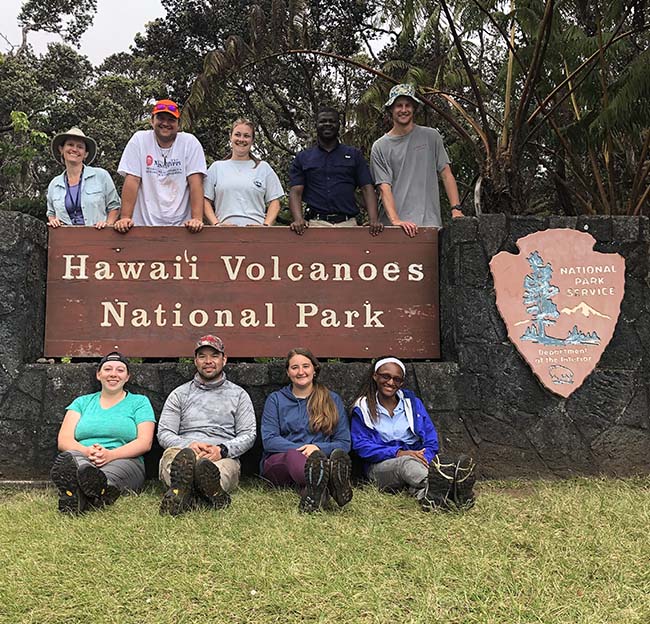 students posing with the Hawaii Volcanoes National Park sign.