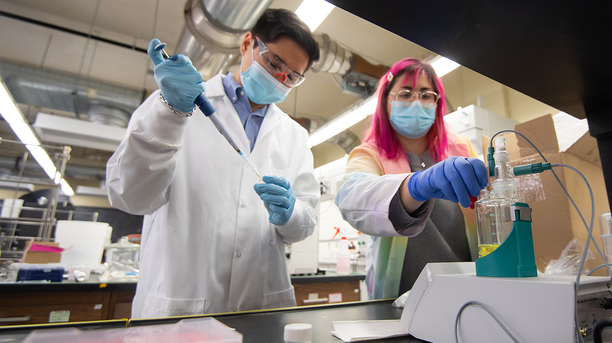 male and female student working in a chemistry lab with white lab coats and masks