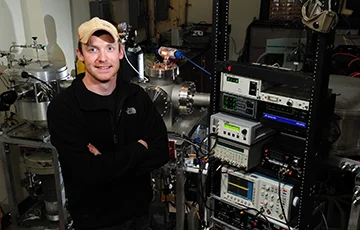 A chemical physics student poses in front of his equipment.