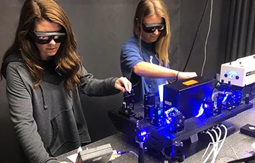 two people using lab equipment emitting bright blue light.