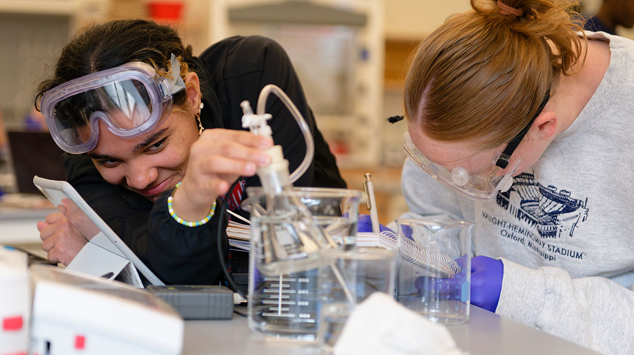 two students in chemistry using tools at a table