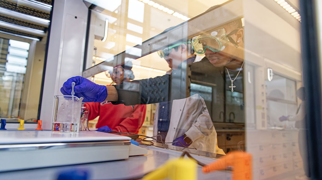 students looking through glass and dropping liquid into a becker