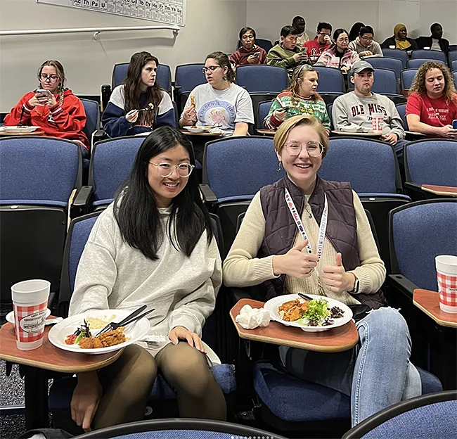 Group of students in auditorium eating food in party atmosphere