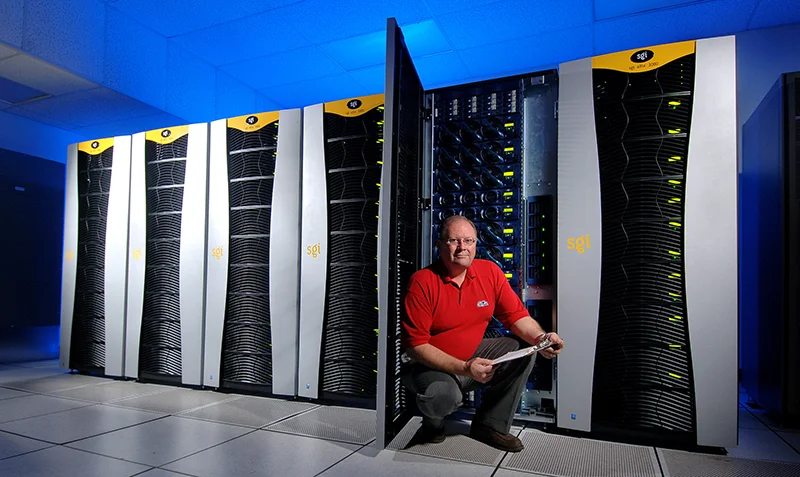 man squatting in front of room-sized computer