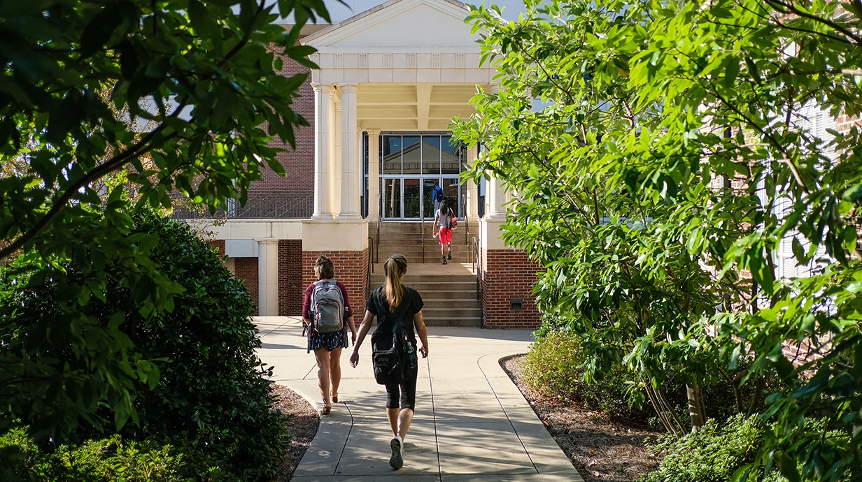 Entrance to brick building (Bishop Hall). Students are walking up the sidewalk toward the building with their back to the camera.