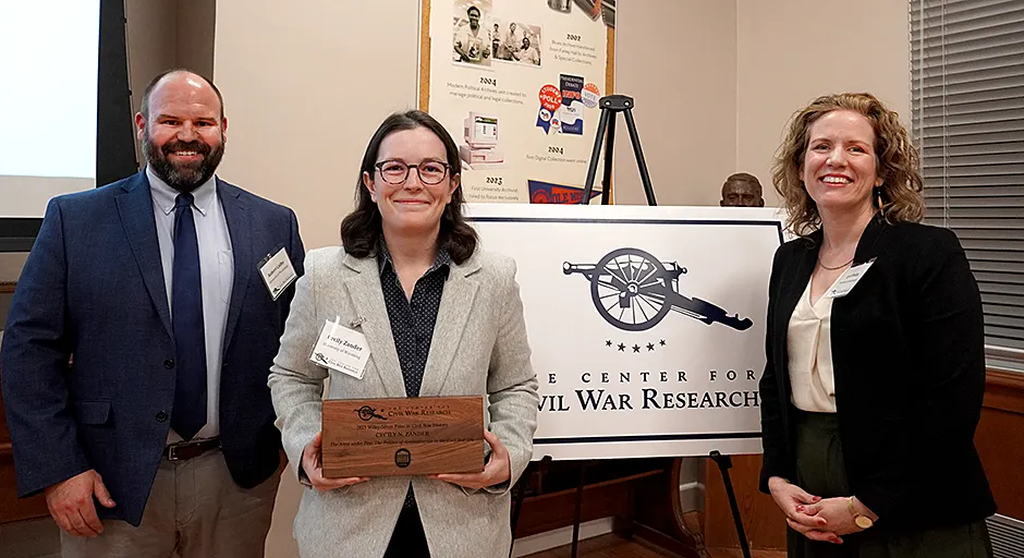 Zander holding book prize; flanked by two smiling people