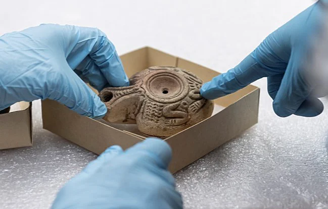 two hands wearing blue latex gloves holding an artifact