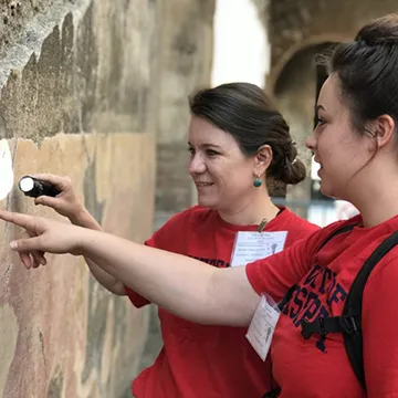 Student and professor inspect wall with flashlight.