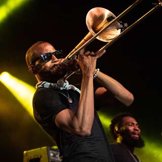 Musician wearing sunglasses on stage playing trombone.