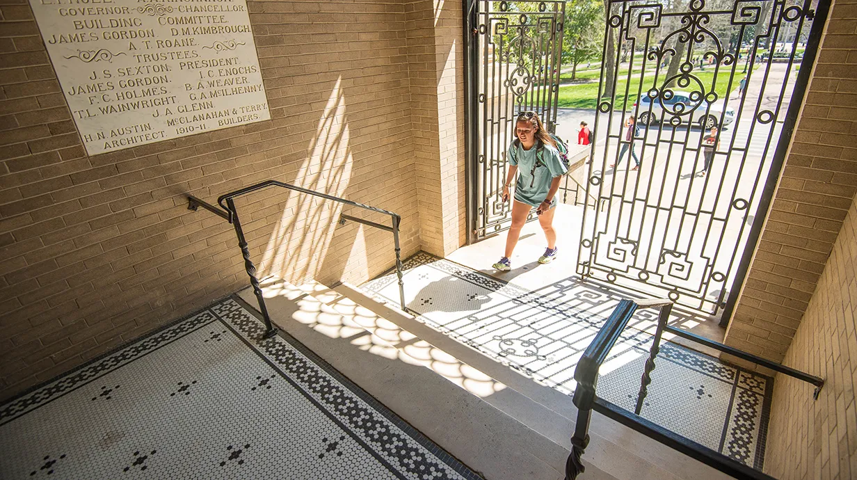 Student walking through an ornate iron door into a foyer with an ornately tiled floor.