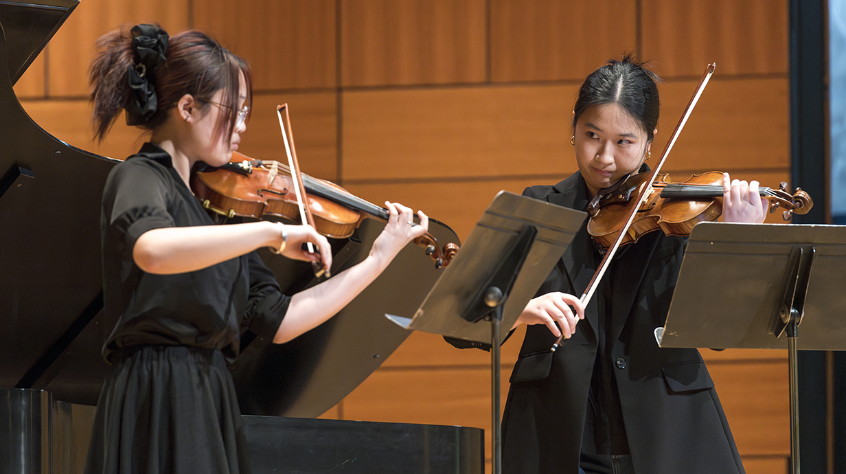 Two girls playing the violins wearing black attire.