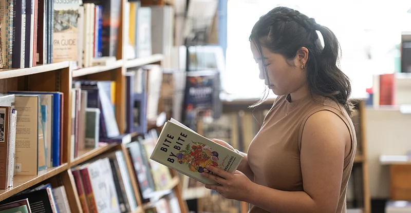 person in profile looking at a book. Books on shelves in background