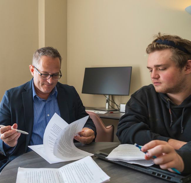 Faculty member Dustin Parsons meeting with student at a desk. They have papers in front of them.