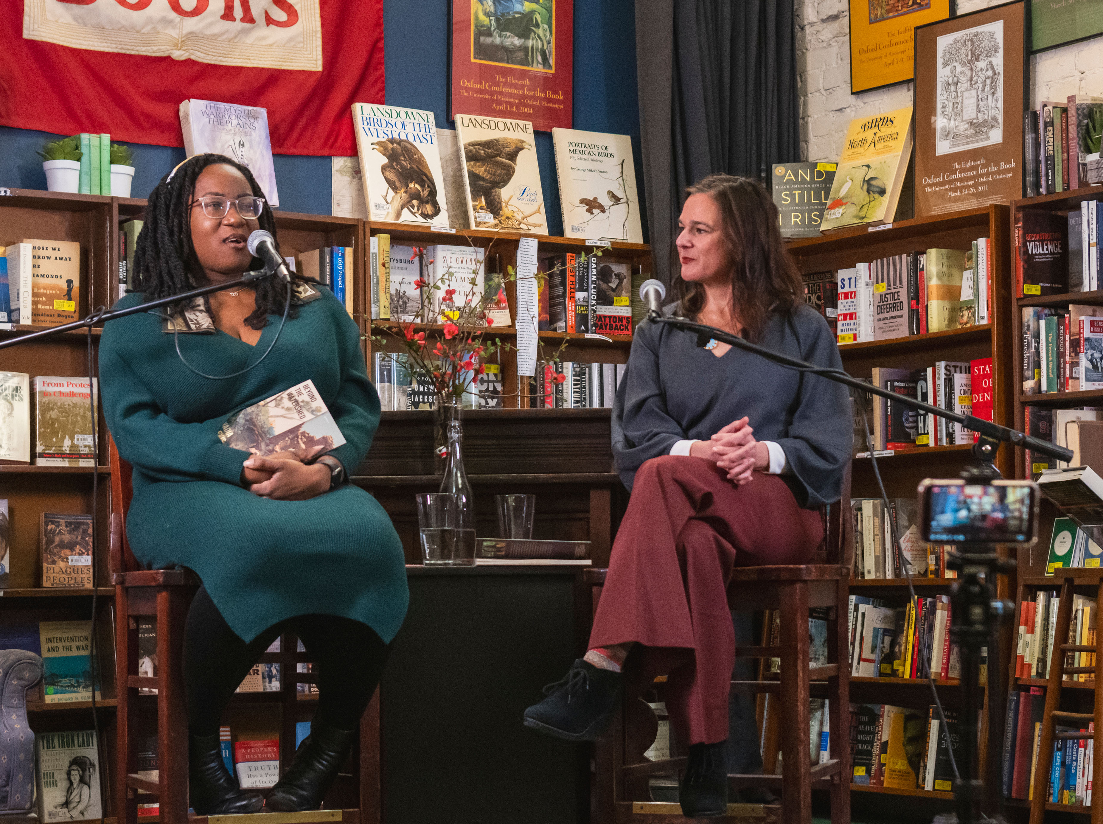 Nadia Alexis and Melissa ginsburg sit in front of bookshelves at square books discussing Alexis' latest release