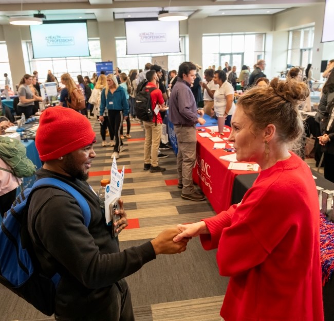 a health professions representative shaking hands with a student  in a large room with many students and health professions representatives