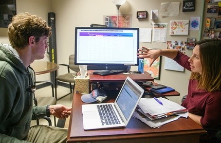 advisor and student seated together in an office and looking at a computer screen