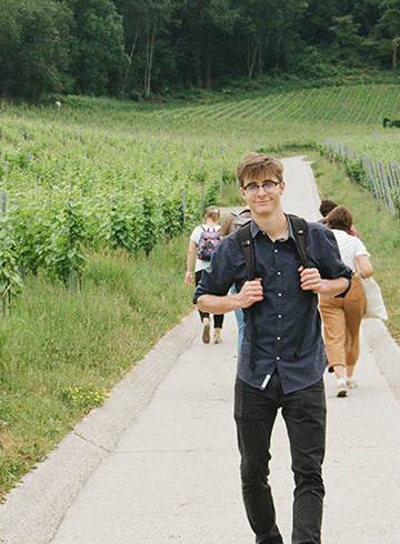 male student standing among a green farm field