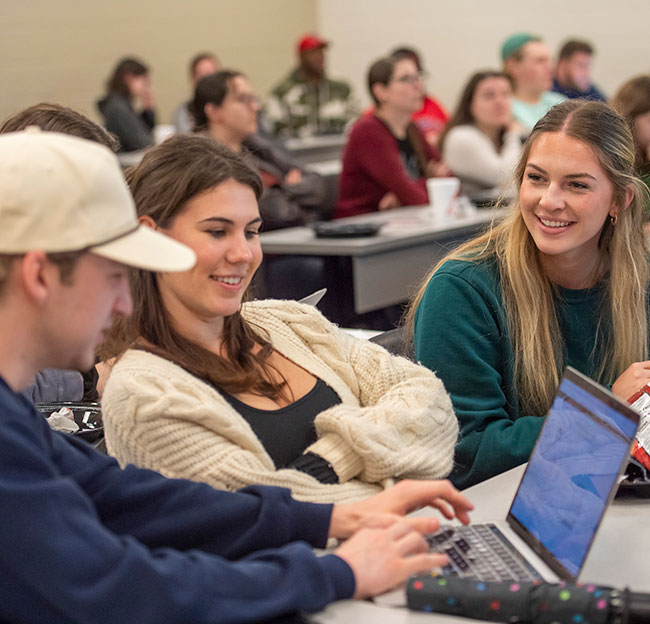 three students sit with computers and smile while discussing
