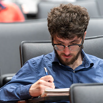 male student with glasses taking notes in notebook