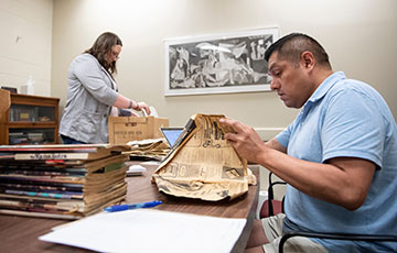female student standing and male student sitting while going through historical documents