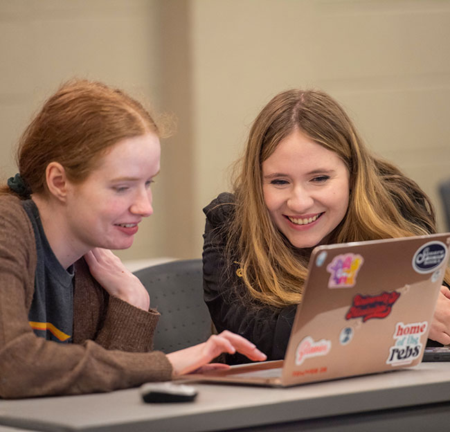 two female students smile at a computer screen