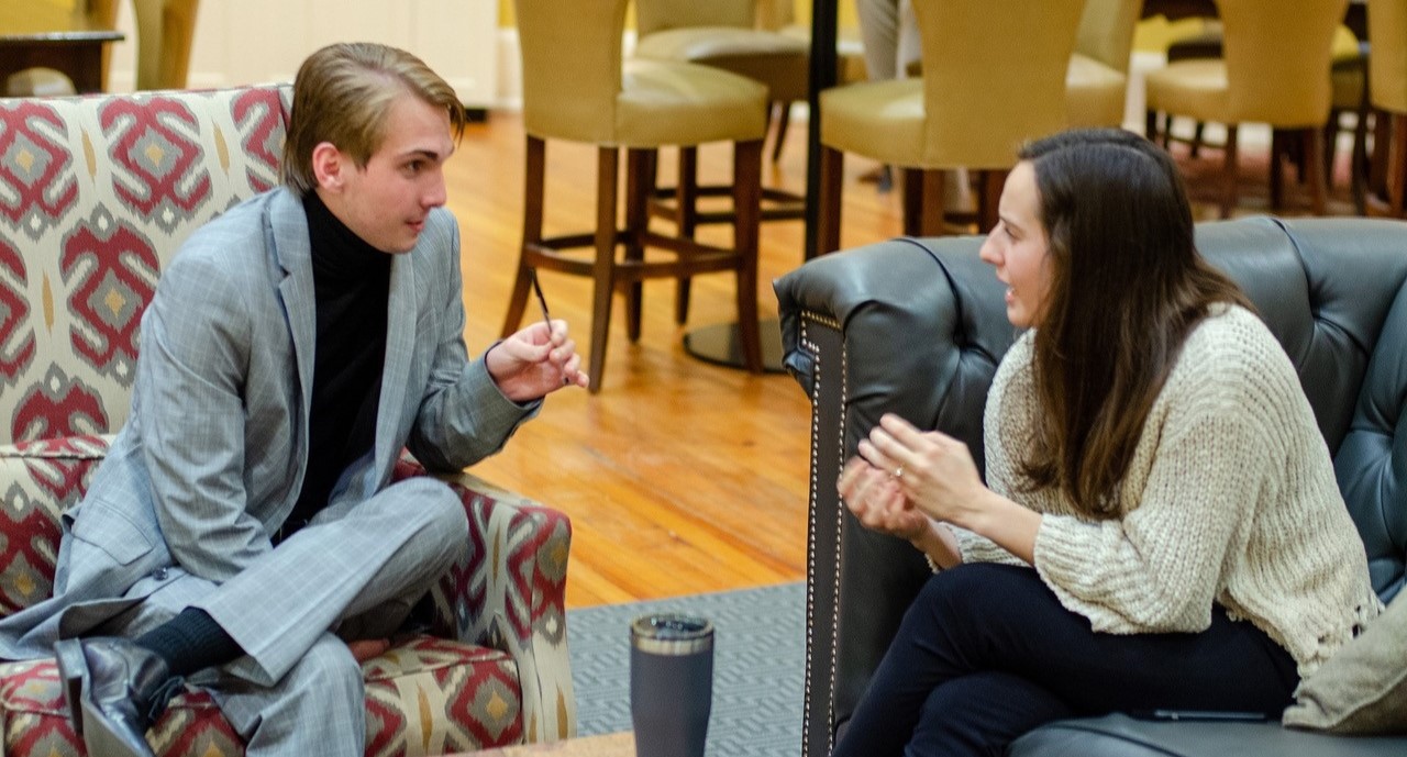 image of two students sitting and talking with each other in the lobby of a building