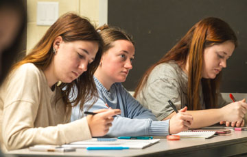 three female students writing in notebooks at a desk