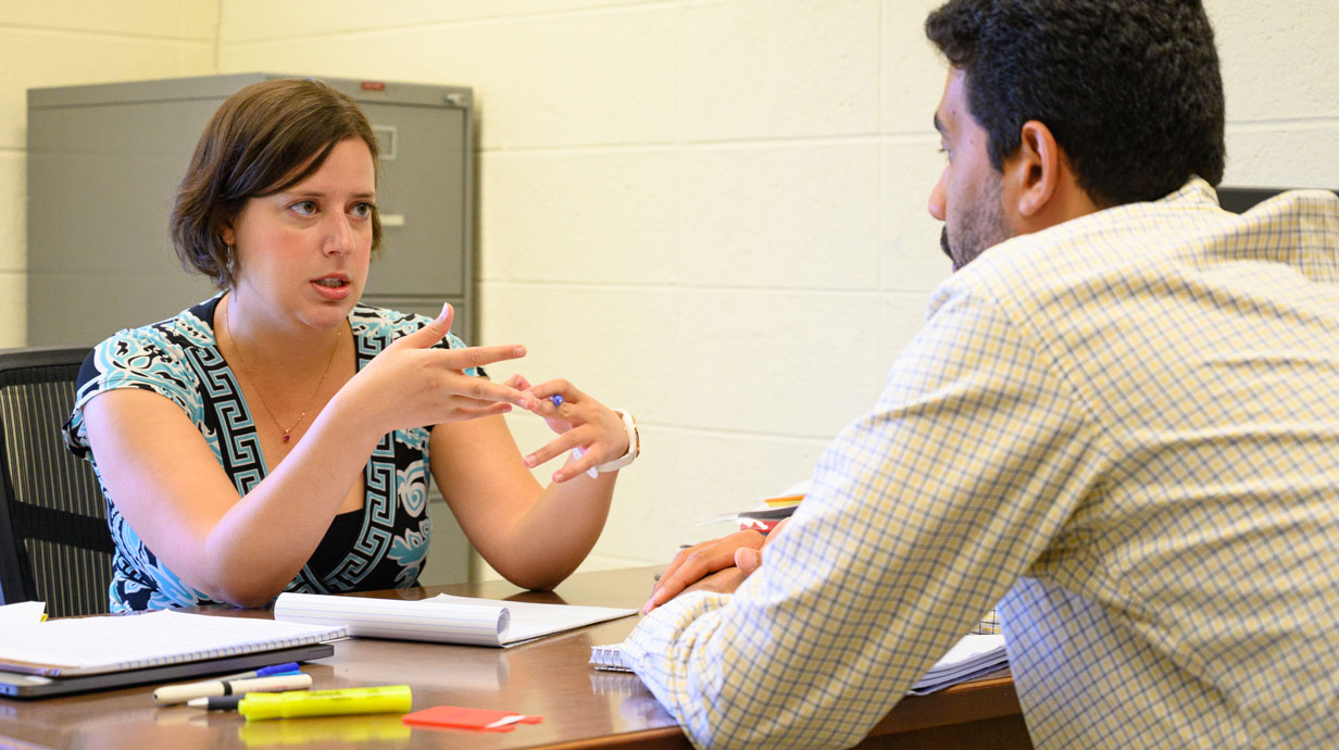 female professor sitting at a desk and talking with a student