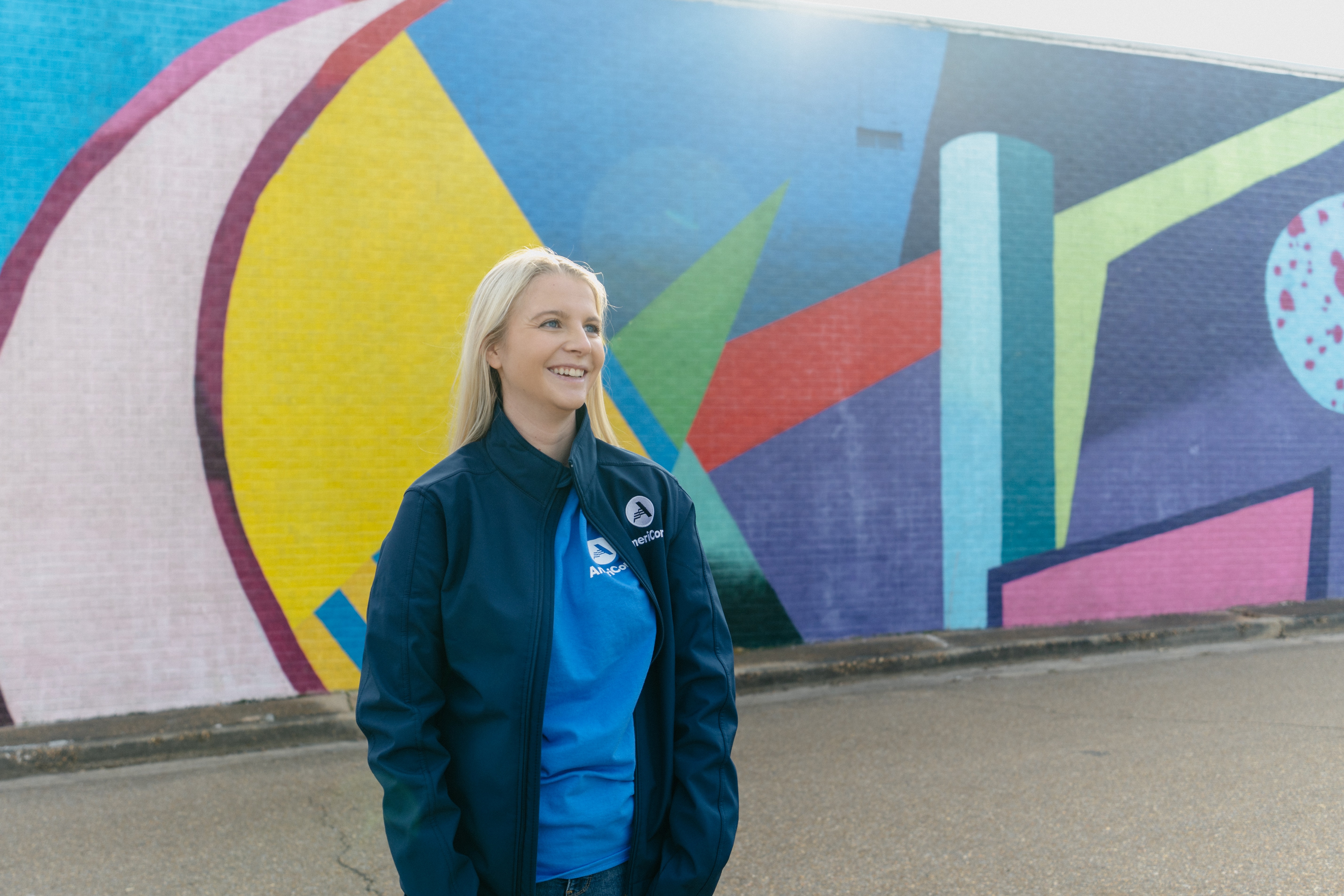 AmeriCorps member, Carrie, stares into the distance in front of a colorful mural