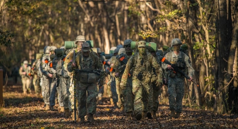 image of a group of cadets jogging in formation through the woods carrying training guns