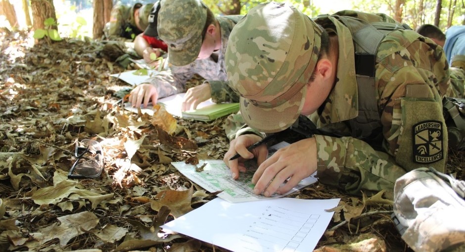 small group of cadets are hunched over studying maps while in a woods