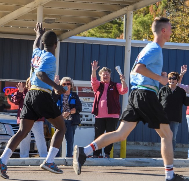 cadets running through town on egg bowl run and waving at people lined along the route