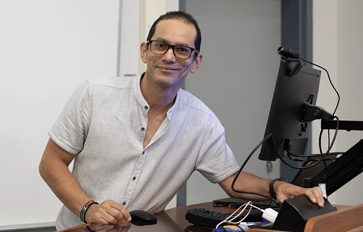 professor leaning on podium with computer monitor and other equipment