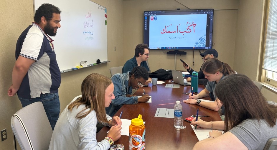 small group of students seated at a conference table studying together with a professor standing nearby