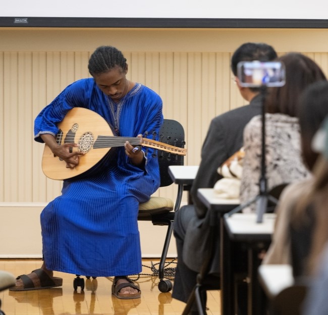 image of a man in blue traditional Arabic clothing playing a guitar in front of a crowd