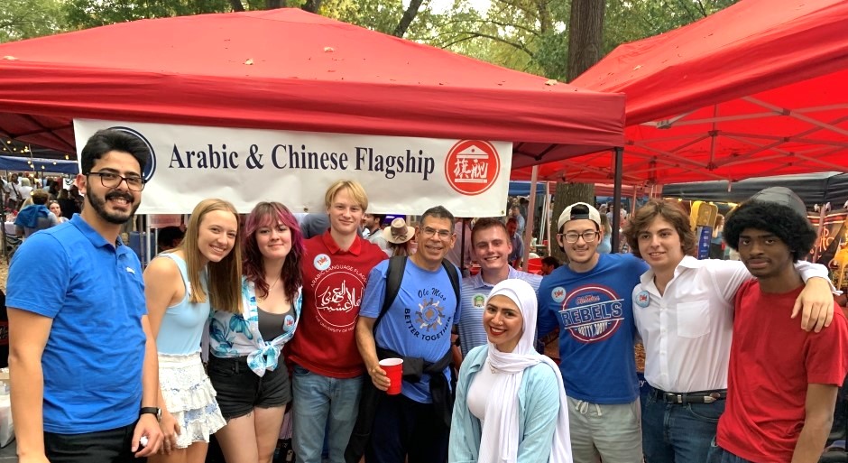 students gathered together and smiling at the camera with an Ole Miss Grove tent behind them