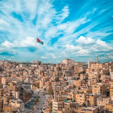 aerial view of Amman, Jordan, with many adobe buildings and a large flagpole with the Jordanian flag.