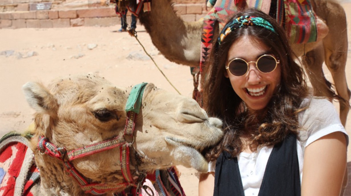 camel is nuzzling a student's shoulder as she smiles