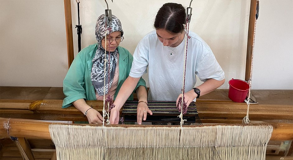 student and an older woman work at a traditional loom