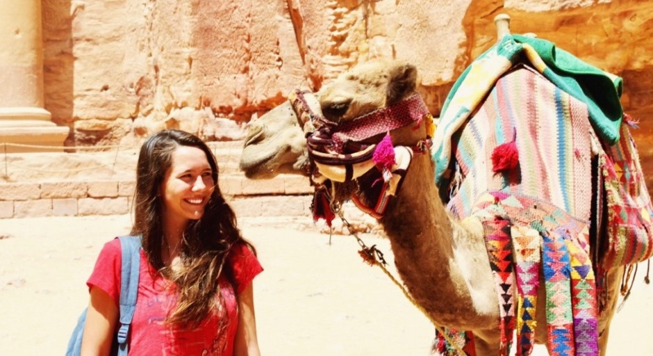 student standing next to a camel that is looking at her up close