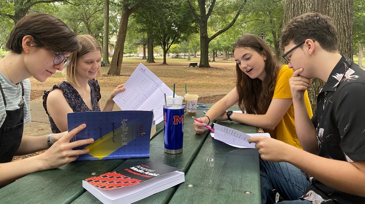 image of four students seated around a picnic table in the Grove studying together