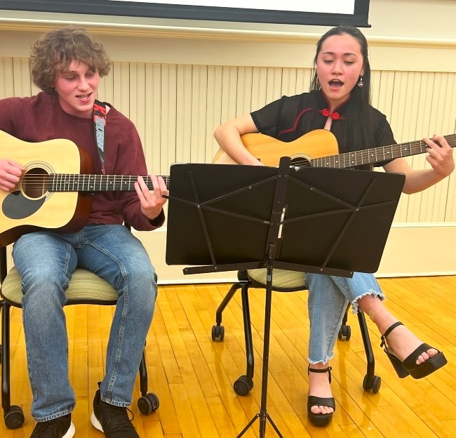 image of two students playing guitar and singing in front of a crowd