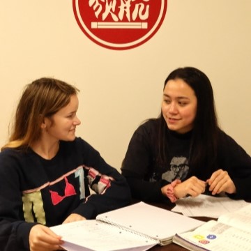 two students seated at a table together with notebooks and books in front of them