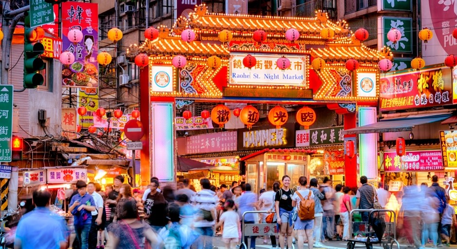 image of a street at night with many people entering through an elaborate Chinese architecture gate 