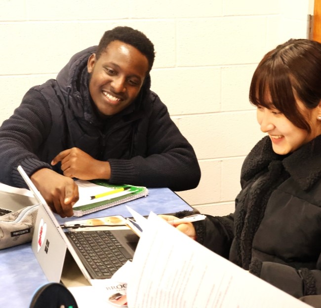 two students seated together, with one pointing at a computer screen