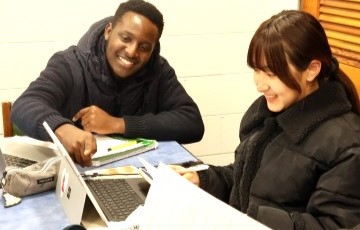 two students working together at a table and pointing to a computer screen