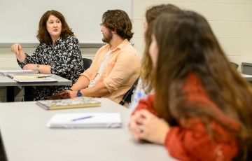 three students and a professor seated together talking and smiling in a classroom